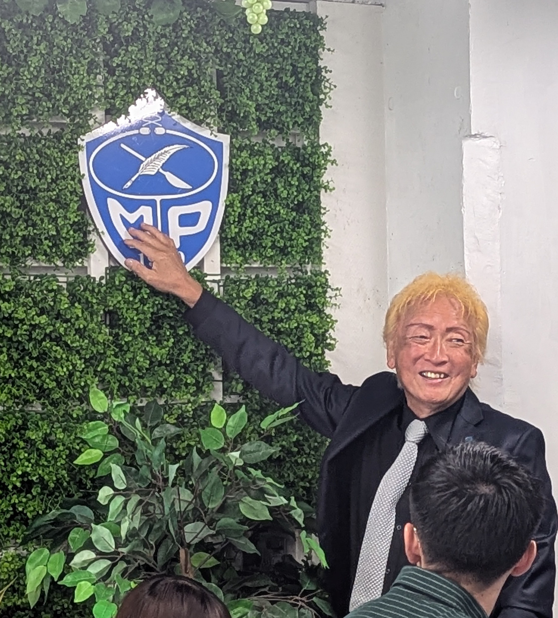 校章に手を添えて微笑む長澤潔志代表